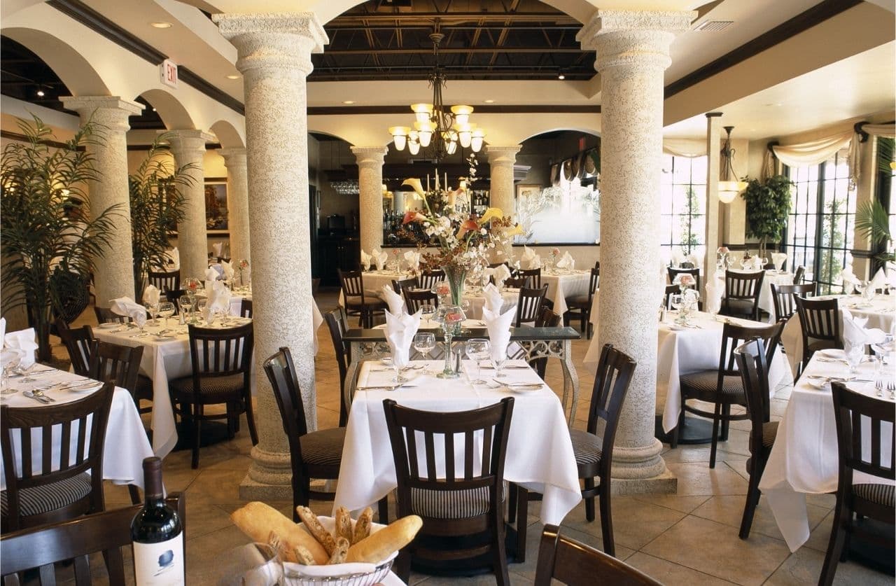 Josephine's of Boca elegant main dining room with stone columns, white linen tables, and chandelier